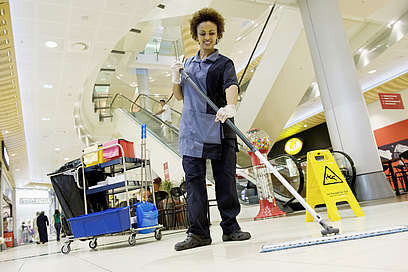 Eine Frau reinigt in einme Supermarkt mit einem Mop den Boden.